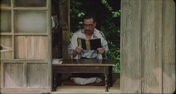 Movie still from “Madadayo” (1993), directed by Akira Kurosawa – A man sitting on the ground reading a book; Medium shot, High angle