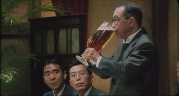 Movie still from “Madadayo” (1993), directed by Akira Kurosawa – A man in a suit is holding up a glass of beer; Medium shot, Low angle
