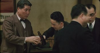 Movie still from “Madadayo” (1993), directed by Akira Kurosawa – A man holding a bottle of beer in his hand while another man looks on; Medium shot, Over the shoulder angle