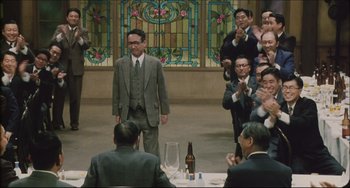 Movie still from “Madadayo” (1993), directed by Akira Kurosawa – A group of people sitting at a table with a man in a suit; Wide shot, Over the shoulder angle