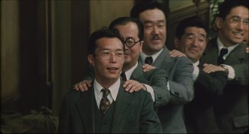 Movie still from “Madadayo” (1993), directed by Akira Kurosawa – A group of men in suits and ties posing for a picture; Medium shot, Low angle