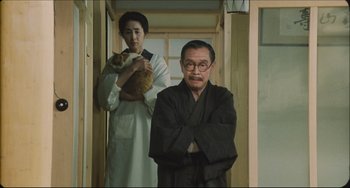 Movie still from “Madadayo” (1993), directed by Akira Kurosawa – An old man and a young woman standing in front of a door; Medium shot, Low angle