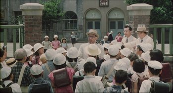 Movie still from “Madadayo” (1993), directed by Akira Kurosawa – A group of people wearing white hats standing in front of a building; Medium shot, Low angle