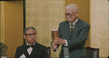 Movie still from “Madadayo” (1993), directed by Akira Kurosawa – An older man holding a glass of beer in front of an older man; Medium shot, Low angle
