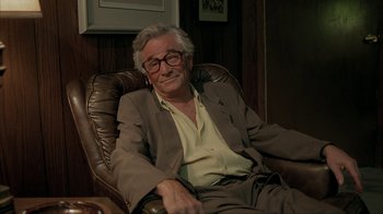 Movie still from “Made” (2001), directed by Jon Favreau – An older man sitting in a chair with his eyes closed; Medium shot, High angle