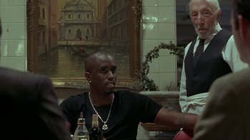 Movie still from “Made” (2001), directed by Jon Favreau – A man sitting in front of a painting at a restaurant; Medium shot, Over the shoulder angle