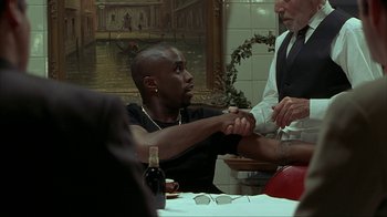 Movie still from “Made” (2001), directed by Jon Favreau – A man sitting at a table with another man holding his hands; Medium shot, Over the shoulder angle