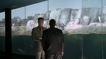 Movie still from “Made” (2001), directed by Jon Favreau – Two men are standing in front of a large screen; Medium shot, Over the shoulder angle