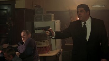 Movie still from “Made” (2001), directed by Jon Favreau – A man in a suit and tie holding a gun in a room; Medium shot, Over the shoulder angle