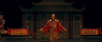 Movie still from “Magic in the Moonlight” (2014), directed by Woody Allen – A man dressed in oriental clothing holding a sword in front of an asian building; Wide shot, Low angle