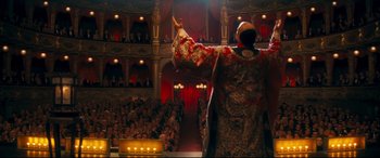 Movie still from “Magic in the Moonlight” (2014), directed by Woody Allen – A man in a red and white robe is on stage; Wide shot, High angle