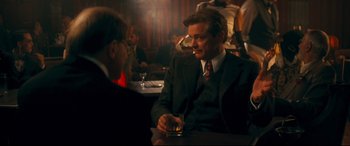 Movie still from “Magic in the Moonlight” (2014), directed by Woody Allen – A man sitting at a table with a drink in his hand; Medium shot, Over the shoulder angle