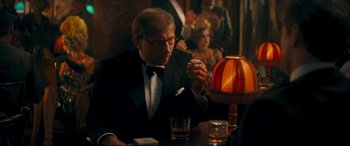 Movie still from “Magic in the Moonlight” (2014), directed by Woody Allen – An older man sitting at a table in front of a lamp; Medium shot, Over the shoulder angle