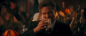 Movie still from “Magic in the Moonlight” (2014), directed by Woody Allen – A man in a suit and tie drinking a glass of whiskey; Close Up shot, Over the shoulder angle