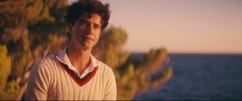 Movie still from “Magic in the Moonlight” (2014), directed by Woody Allen – A man in a white sweater standing in front of trees; Close Up shot, Over the shoulder angle