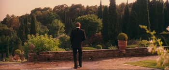 Movie still from “Magic in the Moonlight” (2014), directed by Woody Allen – A man in a suit standing in front of trees; Wide shot, Over the shoulder angle