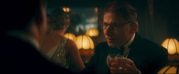 Movie still from “Magic in the Moonlight” (2014), directed by Woody Allen – A man in a suit is holding a drink; Close Up shot, Over the shoulder angle