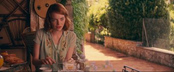 Movie still from “Magic in the Moonlight” (2014), directed by Woody Allen – A woman sitting at a table with a glass of tea; Medium shot, Over the shoulder angle