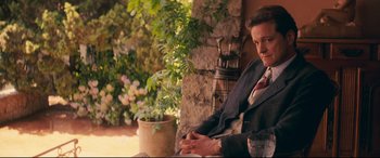 Movie still from “Magic in the Moonlight” (2014), directed by Woody Allen – A man in a suit sitting on a chair outside; Medium shot, Over the shoulder angle