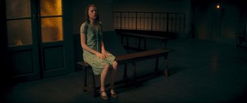 Movie still from “Magic in the Moonlight” (2014), directed by Woody Allen – A woman sitting on top of a wooden bench in a room; Wide shot, High angle