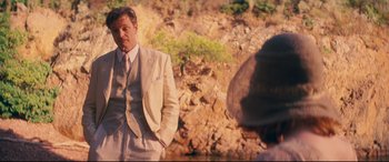 Movie still from “Magic in the Moonlight” (2014), directed by Woody Allen – A man in a suit and tie standing in front of a stone wall; Medium shot, Over the shoulder angle