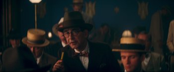 Movie still from “Magic in the Moonlight” (2014), directed by Woody Allen – An older man in a suit and hat holding a banana; Medium shot, Over the shoulder angle