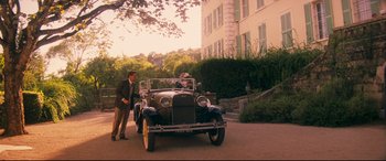 Movie still from “Magic in the Moonlight” (2014), directed by Woody Allen – An old car is parked in front of a building; Wide shot, High angle