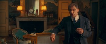 Movie still from “Magic in the Moonlight” (2014), directed by Woody Allen – A man wearing a suit and tie in a room; Medium shot, Over the shoulder angle