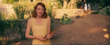 Movie still from “Magic in the Moonlight” (2014), directed by Woody Allen – A woman in a yellow dress holding a book; Medium shot, Over the shoulder angle