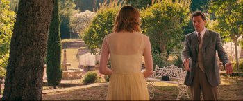 Movie still from “Magic in the Moonlight” (2014), directed by Woody Allen – A woman in a yellow dress standing in a yard; Wide shot, Over the shoulder angle