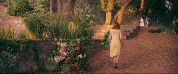 Movie still from “Magic in the Moonlight” (2014), directed by Woody Allen – A woman in a yellow dress walking down a path in a garden; Wide shot, High angle