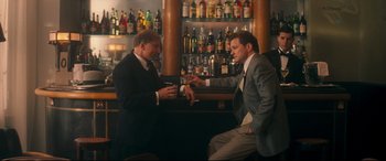 Movie still from “Magic in the Moonlight” (2014), directed by Woody Allen – Two men in suits sitting at a bar drinking; Medium shot, Over the shoulder angle