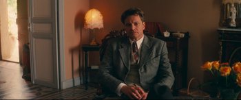 Movie still from “Magic in the Moonlight” (2014), directed by Woody Allen – A man in a suit and tie sitting in a chair; Medium shot, Over the shoulder angle