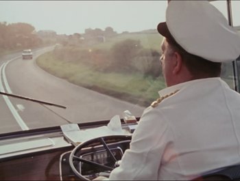Movie still from “Magical Mystery Tour” (1967), directed by Ringo Starr – A man driving a car on a road; Wide shot, High angle