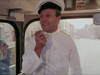 Movie still from “Magical Mystery Tour” (1967), directed by Ringo Starr – A man in a white uniform holding a microphone in his hand; Medium shot, Low angle