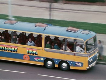 Movie still from “Magical Mystery Tour” (1967), directed by Ringo Starr – A tour bus driving down a street with a bunch of people in it; Wide shot, High angle