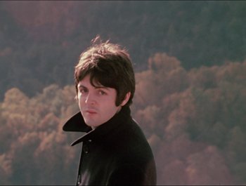 Movie still from “Magical Mystery Tour” (1967), directed by Ringo Starr – A young man in a black jacket standing in front of trees; Close Up shot, High angle