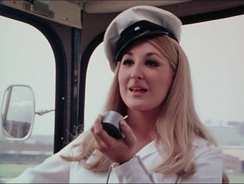 Movie still from “Magical Mystery Tour” (1967), directed by Ringo Starr – A woman holding a cell phone while wearing a hat; Close Up shot, Low angle