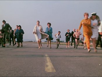 Movie still from “Magical Mystery Tour” (1967), directed by Ringo Starr – A group of people running across an airport runway; Extreme Wide shot, High angle