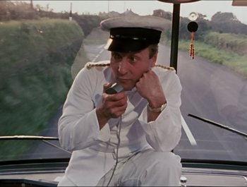 Movie still from “Magical Mystery Tour” (1967), directed by Ringo Starr – A man sitting on a boat holding a cell phone to his ear; Medium shot, High angle