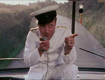 Movie still from “Magical Mystery Tour” (1967), directed by Ringo Starr – A man in a white uniform holding a microphone and pointing; Medium shot, High angle