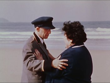 Movie still from “Magical Mystery Tour” (1967), directed by Ringo Starr – An older man and a younger woman embracing on the beach; Medium shot, High angle