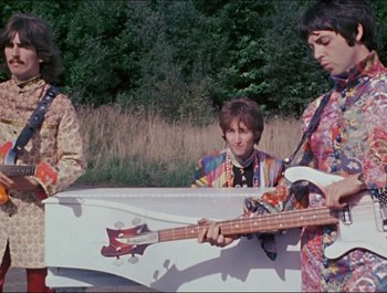 Movie still from “Magical Mystery Tour” (1967), directed by Ringo Starr – A group of young men playing instruments in a field; Wide shot, Low angle