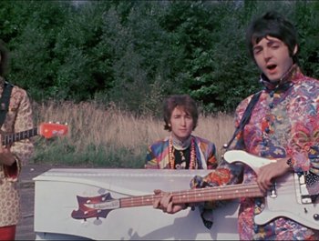 Movie still from “Magical Mystery Tour” (1967), directed by Ringo Starr – Two young men in colorful outfits playing a guitar and a bass guitar; Medium shot, Low angle