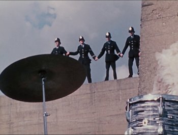 Movie still from “Magical Mystery Tour” (1967), directed by Ringo Starr – A group of men standing on top of a building; Extreme Wide shot, Overhead angle