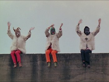 Movie still from “Magical Mystery Tour” (1967), directed by Ringo Starr – A group of people sitting on top of a concrete wall; Wide shot, Low angle