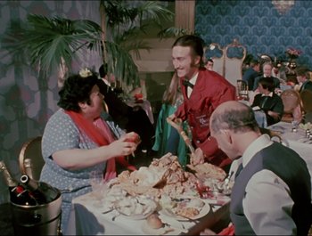 Movie still from “Magical Mystery Tour” (1967), directed by Ringo Starr – A group of people sitting around a table with plates of food on top of it; Medium shot, High angle