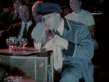 Movie still from “Magical Mystery Tour” (1967), directed by Ringo Starr – An older man smoking a cigarette in front of a group of men; Medium shot, Over the shoulder angle