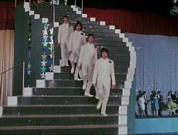 Movie still from “Magical Mystery Tour” (1967), directed by Ringo Starr – A group of men in white suits walking down a set of stairs; Wide shot, High angle