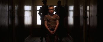 Movie still from “Magnolia” (1999), directed by Paul Thomas Anderson – A young boy standing in front of two other men; Medium shot, Low angle